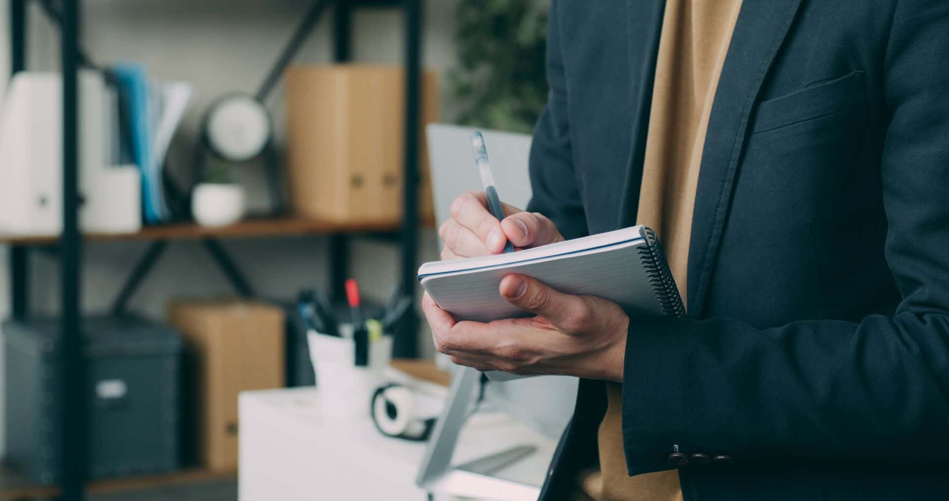 Businessman writing in a notebook in a modern office setting.